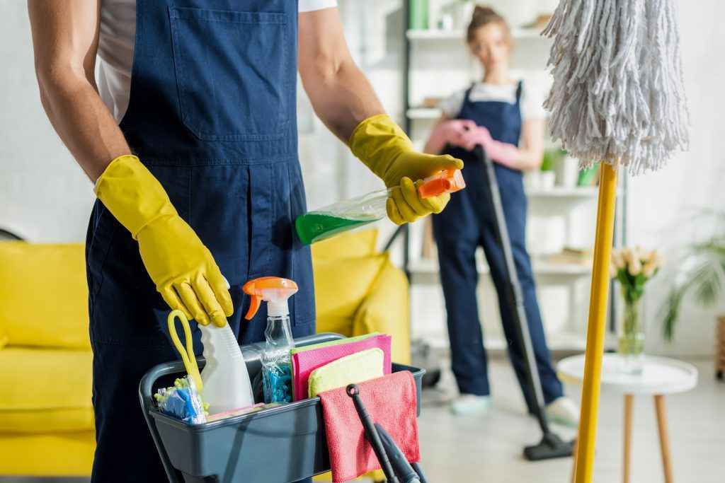 selective focus of cleaner holding spray bottle near cleaning trolley