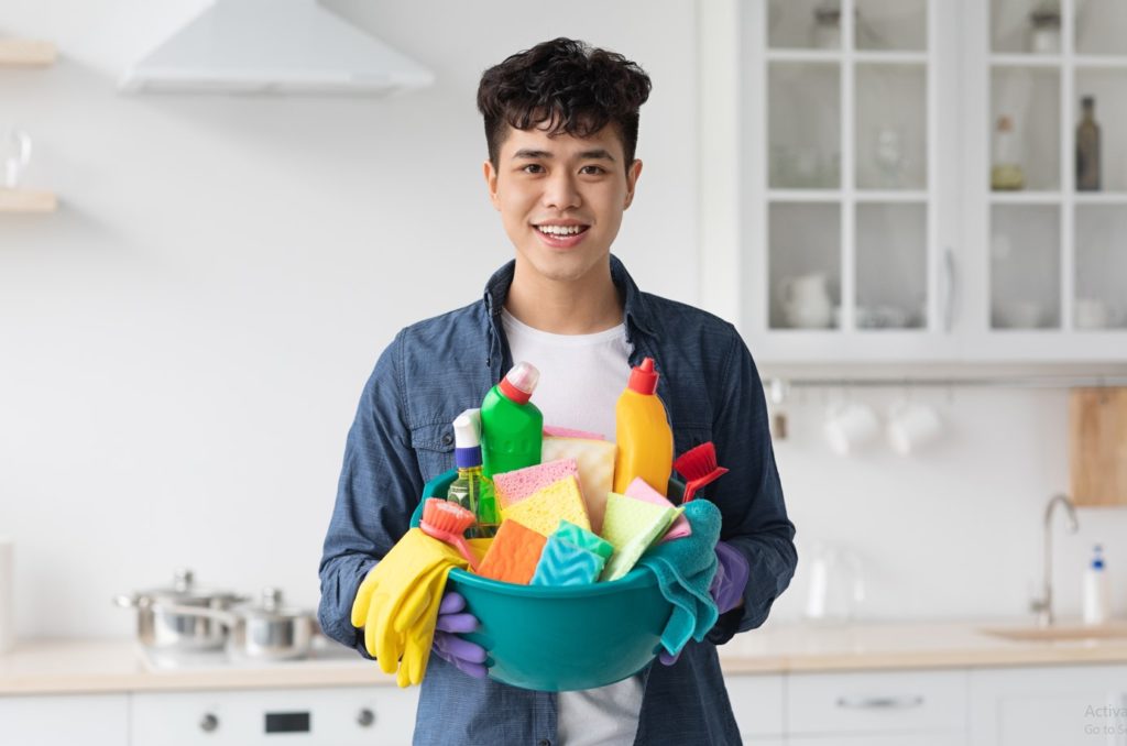 smiling asian guy housekeeper cleaning apartment